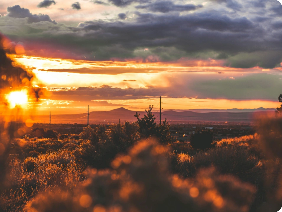 A sunset with clouds and trees in the foreground.