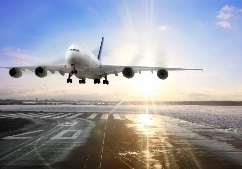 A large airplane flying over an airport runway.